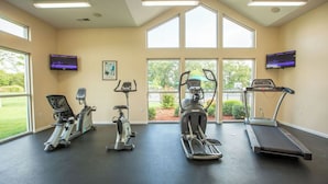 Ein Fitnessraum mit vier Cardiogeräten, großen Fenstern und zwei Fernsehern an den Wänden.