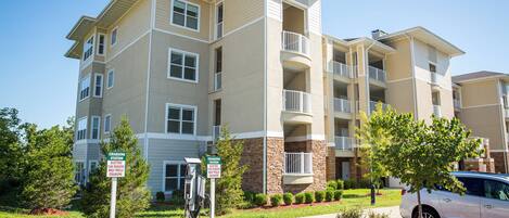 A multi-story apartment building with balconies, a parking area, and a charging station sign.