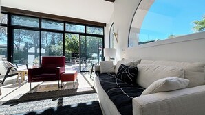 Uma sala de estar moderna com uma janela grande, uma cadeira vermelha, um sofá branco e uma mesinha.