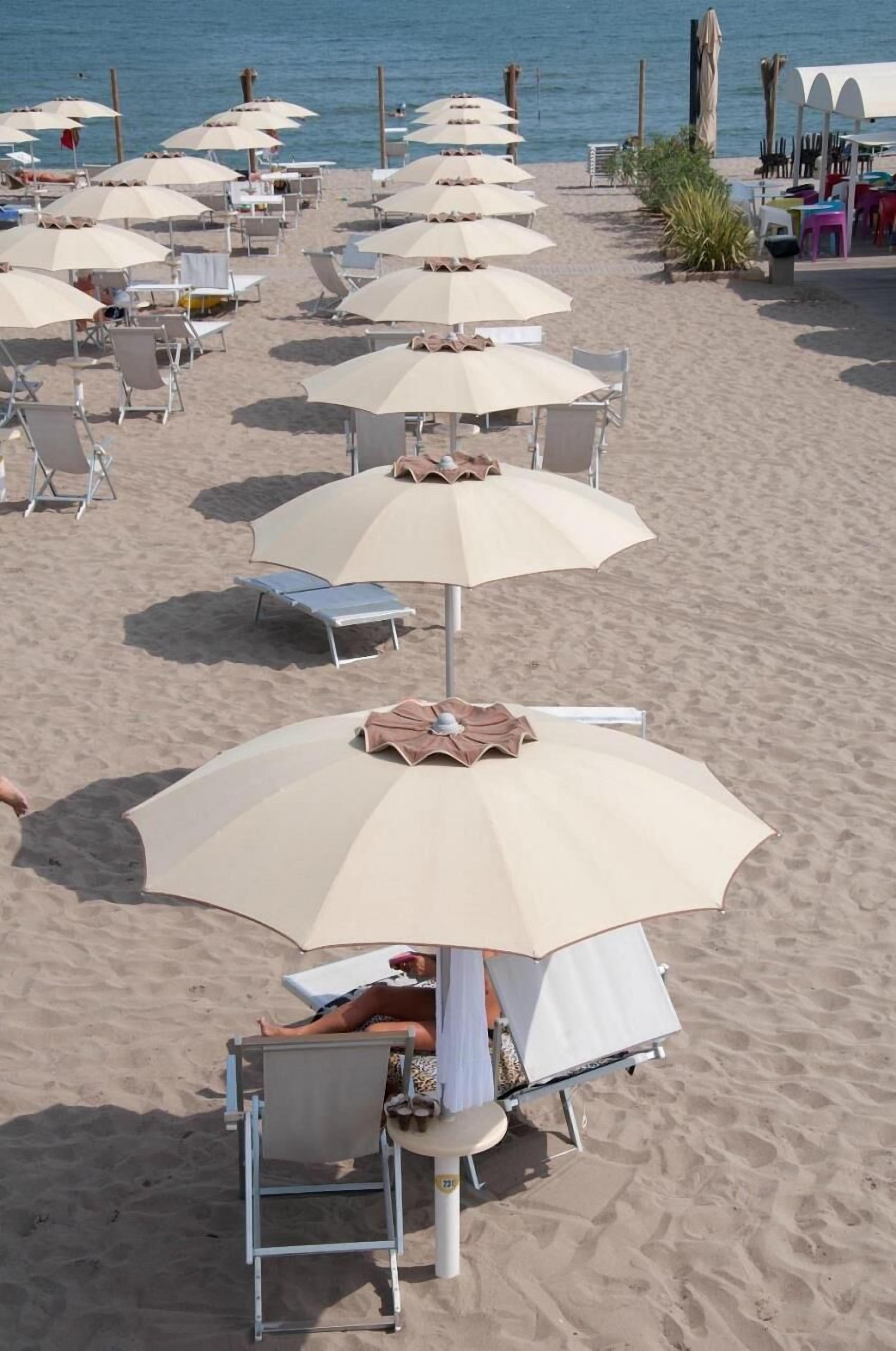 A beach with rows of sun umbrellas and lounge chairs, some occupied by people.