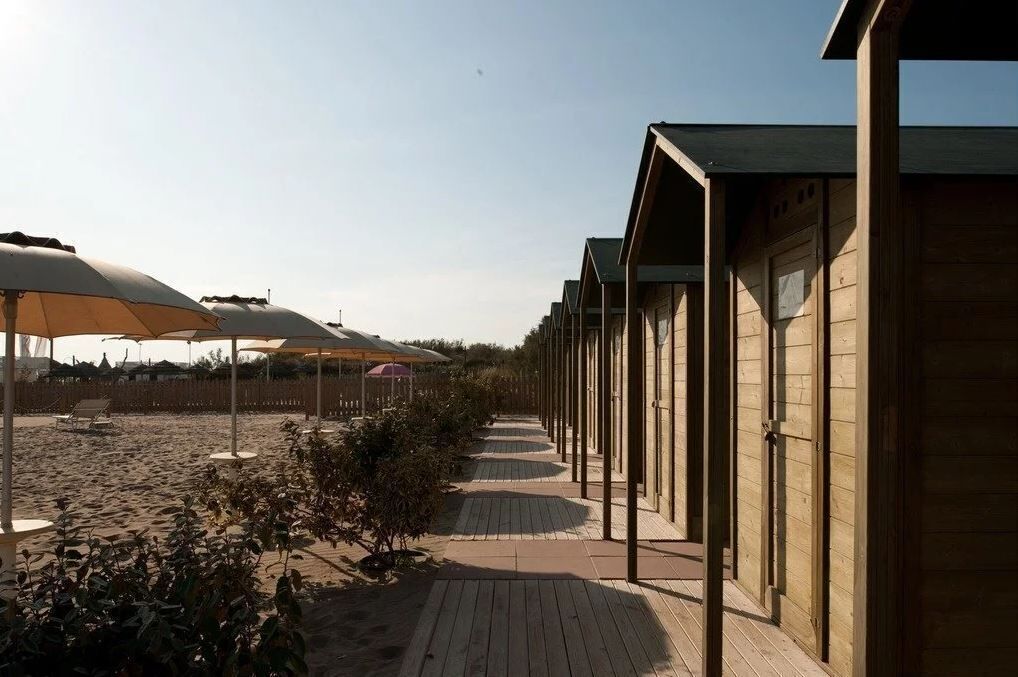 A row of wooden beach huts with a wooden walkway leading to a sandy beach area.