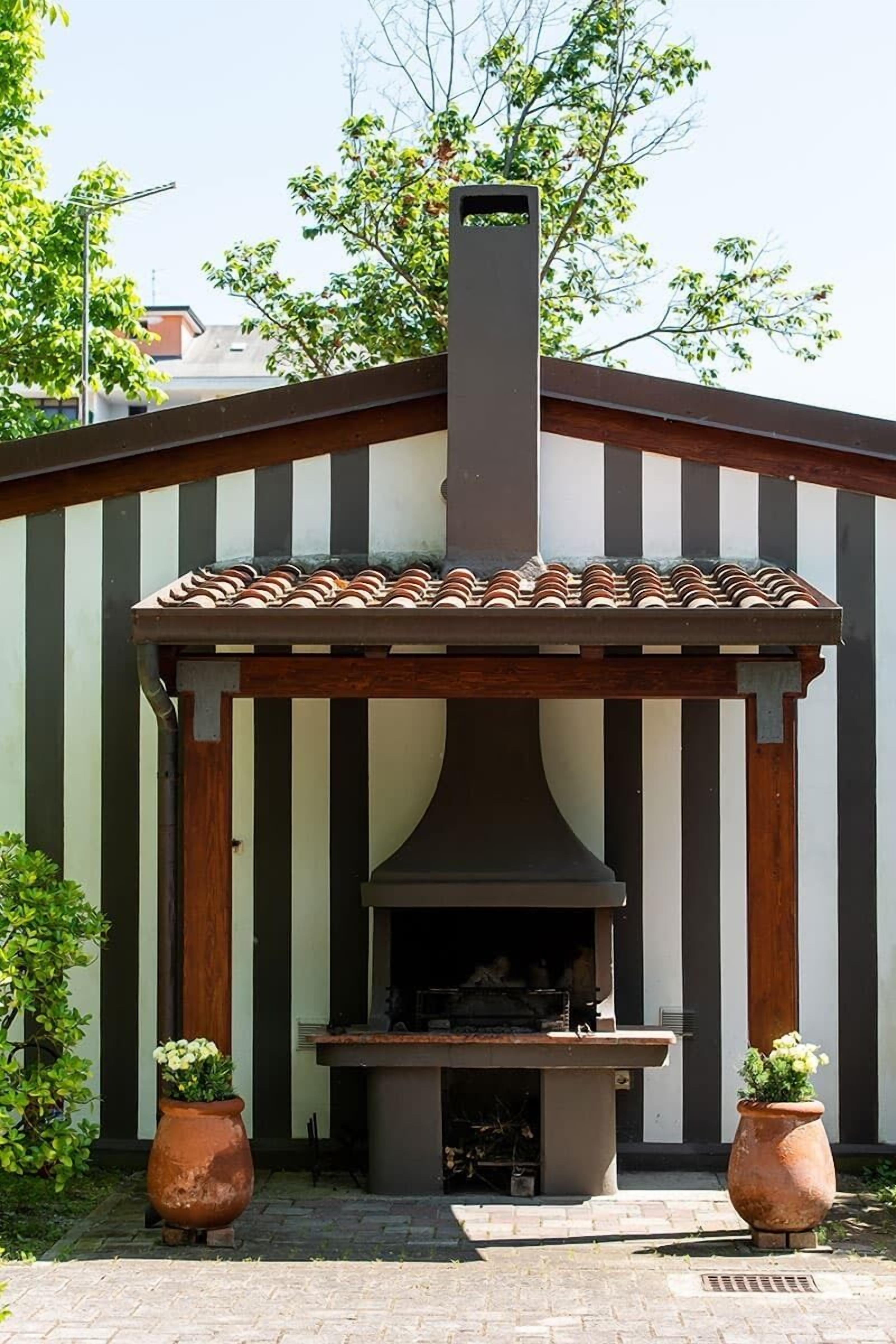 An outdoor kitchen with a chimney, a pergola, and two potted plants.
