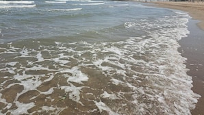 A beach with waves gently lapping onto the shore, a sandy beach, and a rocky breakwater in the distance.