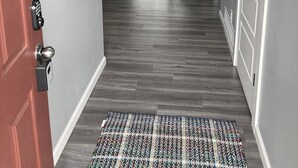 Ein Flur mit Holzboden, grauer Wand, einem Spiegel, einem Kleiderhaken mit Schlüsseln und einer Tür mit Schlüsselsperre.