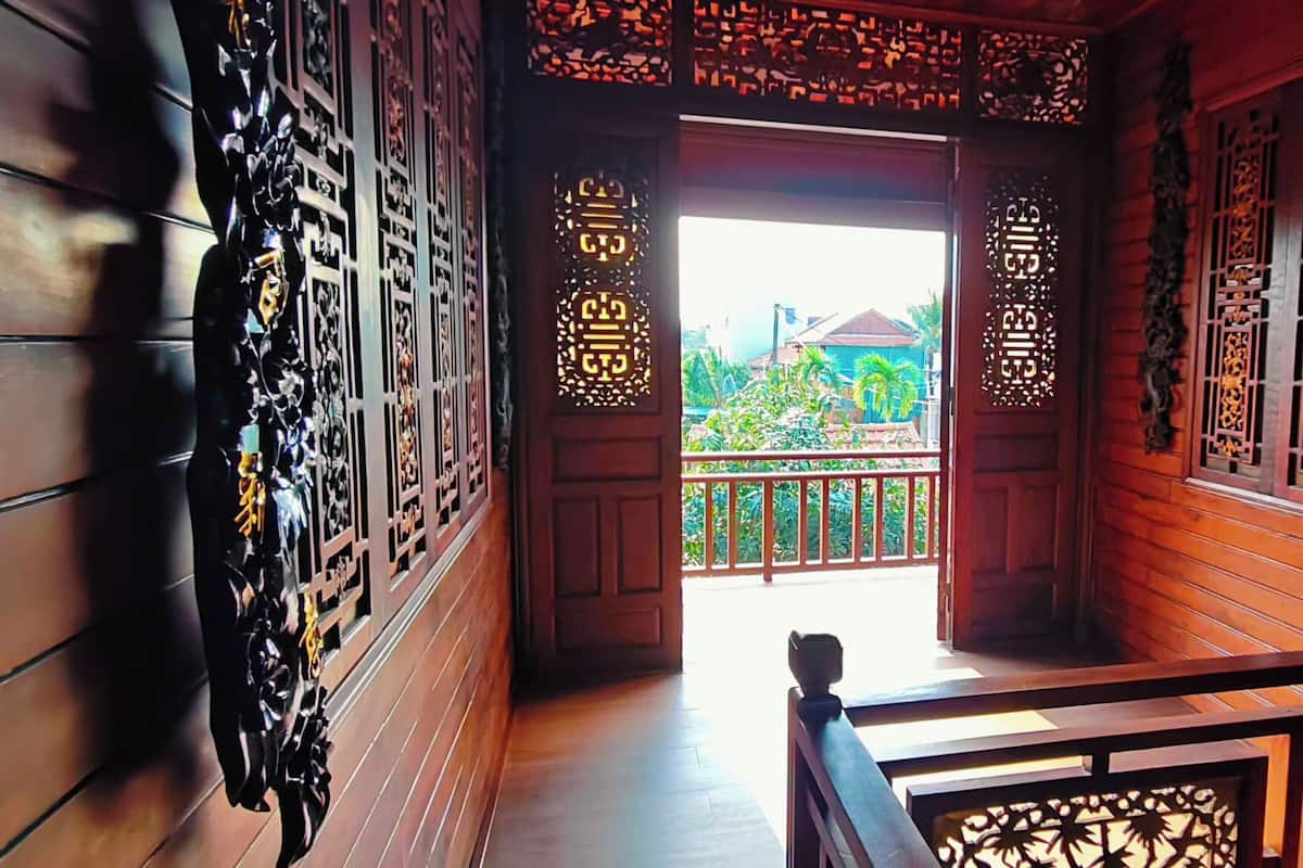A wooden corridor with intricate carvings, a wooden door leading to a balcony, and a railing.