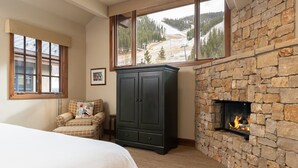A bedroom with a stone fireplace, a bed, a wardrobe, and a window with a mountain view. - Warm Springs 4-bedroom, 4 bath. Gourmet kitchen, fitness room, pool, and hot tub (Ketchum)