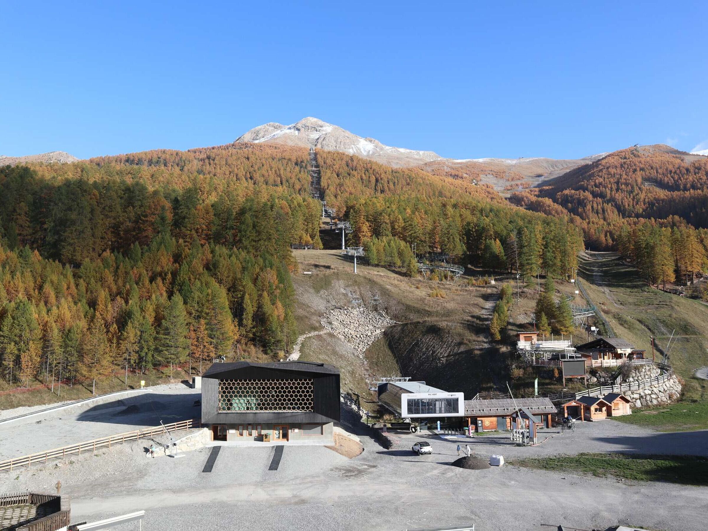 Un chalet de montagne doté d’un bâtiment moderne, d’un télésiège et surplombant une forêt.