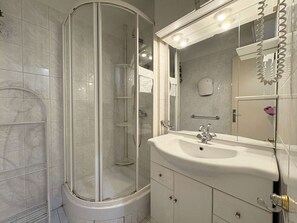 Uma casa de banho moderna com chuveiro envidraçado, lavatório branco e espelho grande com iluminação.
