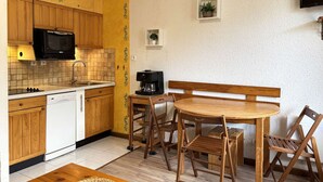 A compact kitchen with wooden cabinets, a microwave, a coffee maker, and a dining table with chairs.