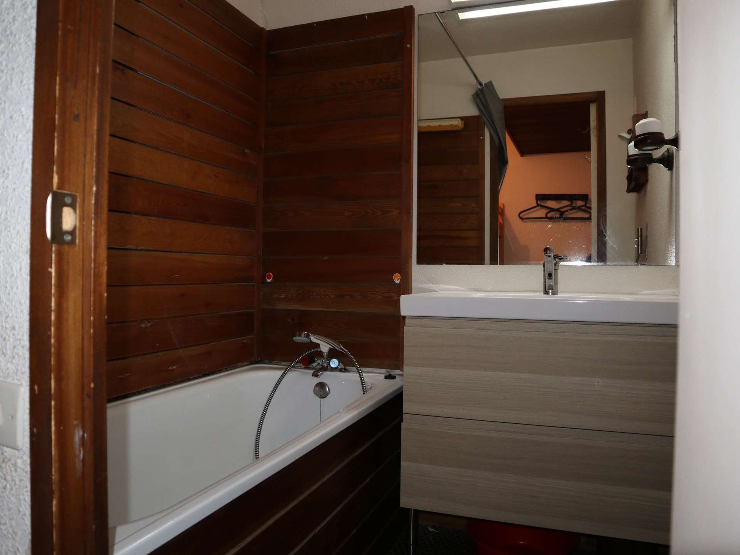 Ein Badezimmer mit Holzwand, einer Badewanne, einem Waschbecken und einem Spiegel.