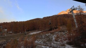 Eine Berglandschaft mit einer Seilbahn, herbstlich gefärbten Bäumen und blauem Himmel.