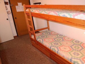 A bunk bed with a patterned mattress, a wooden ladder, and a door with a notice on it.