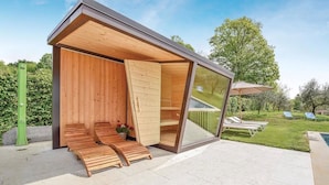 A modern wooden structure with a glass enclosure, wooden benches, and a garden view. - Villa Montello Pool Jacuzzi Ac Wifi  (Volpago del Montello)