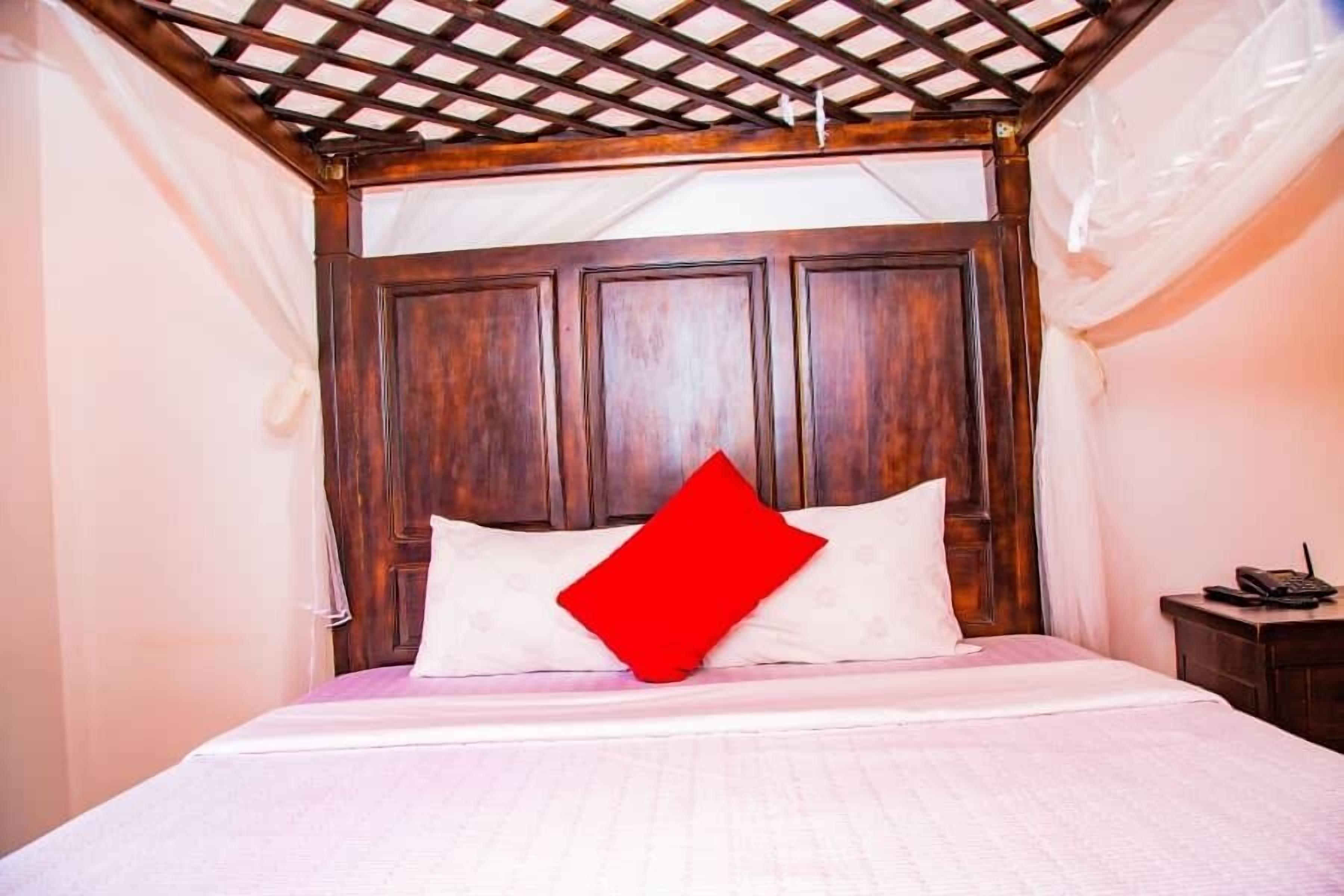 Un lit avec une tête de lit en bois, du linge de lit blanc et un oreiller rouge.