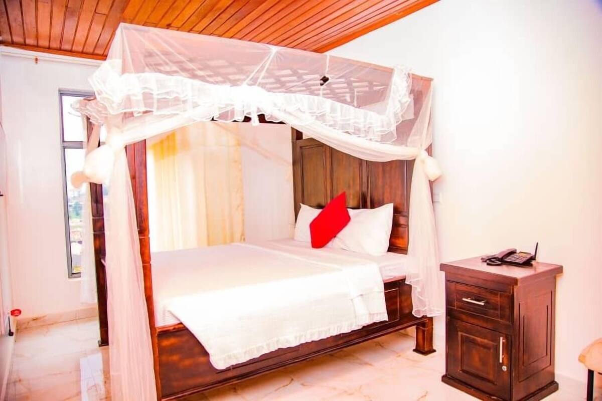 A four-poster canopy bed with white bedding and a red pillow, a wooden nightstand with a phone, and a wooden cabinet.