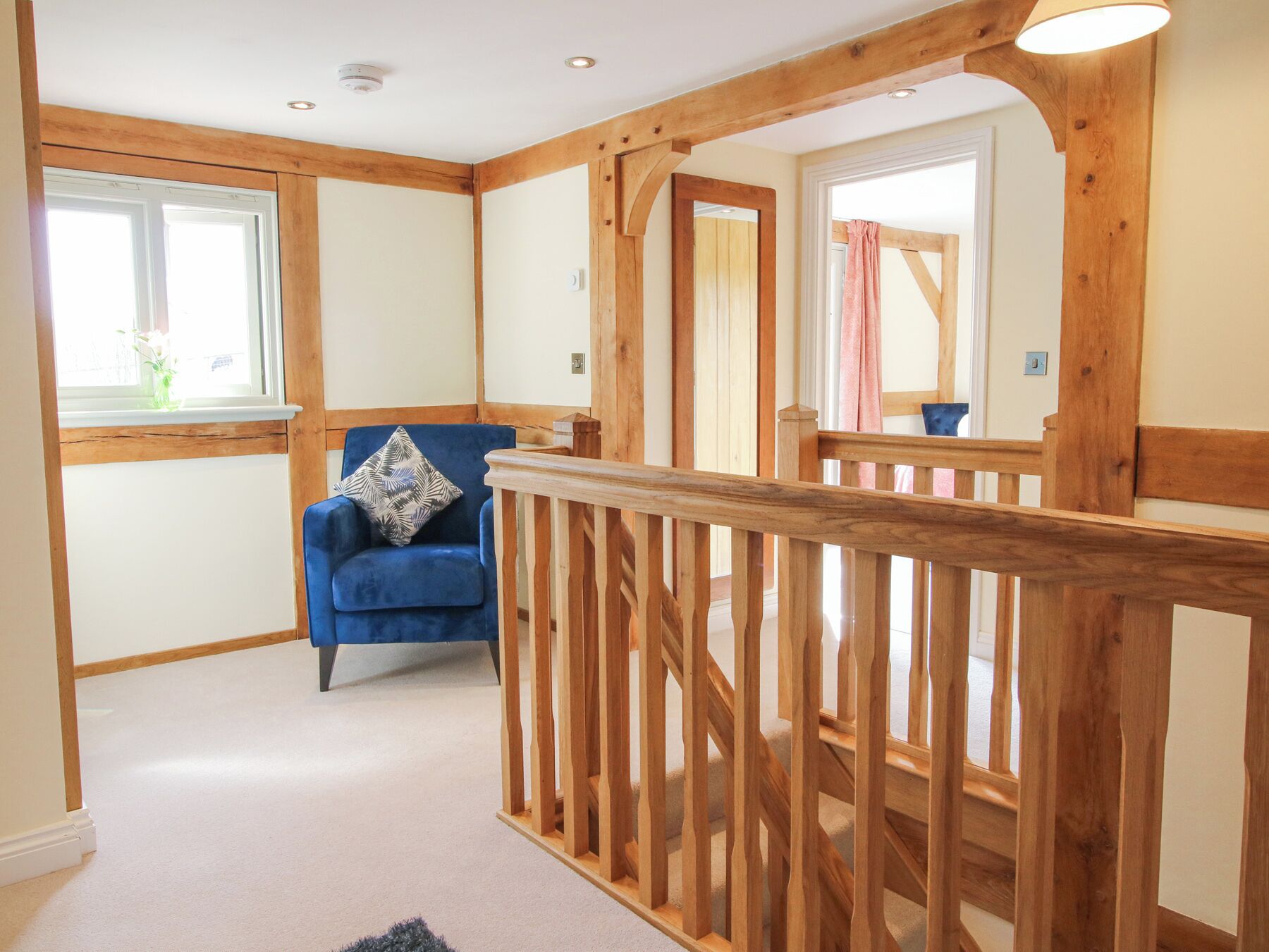 A hallway with wooden beams, a blue chair with a patterned pillow, and a wooden railing.