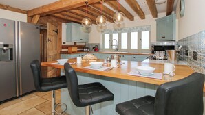 A kitchen with a wooden island, bar stools, a refrigerator, and a sink. - Cuckoo Pen Cottage (Tenbury Wells)