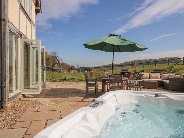 A patio area with a hot tub, outdoor furniture, and a large umbrella. - Cuckoo Pen Cottage (Tenbury Wells)