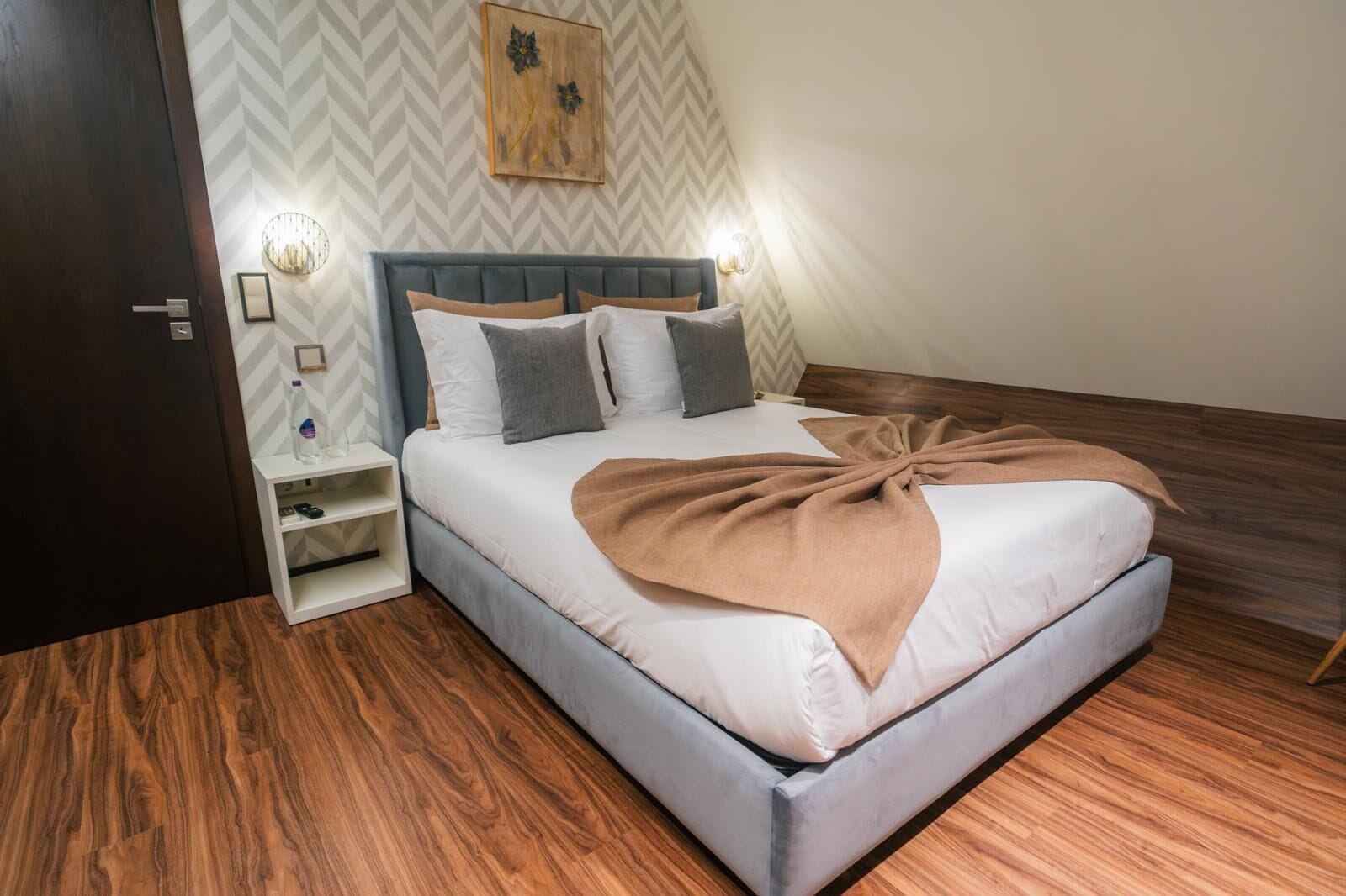 Un dormitorio con una cama, mesitas de noche y suelo de madera.