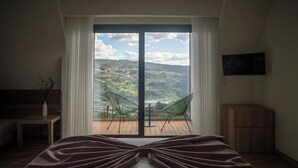 A bedroom with a large bed, a view of the outdoors through a sliding door, a small table with a vase, and a TV mounted on the wall. - Quinta Casal da Silva 1951 (Marco de Canaveses)