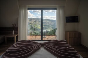 Un dormitorio con una cama grande, vistas al exterior a través de una puerta corredera, una mesita con un florero y un televisor montado en la pared.