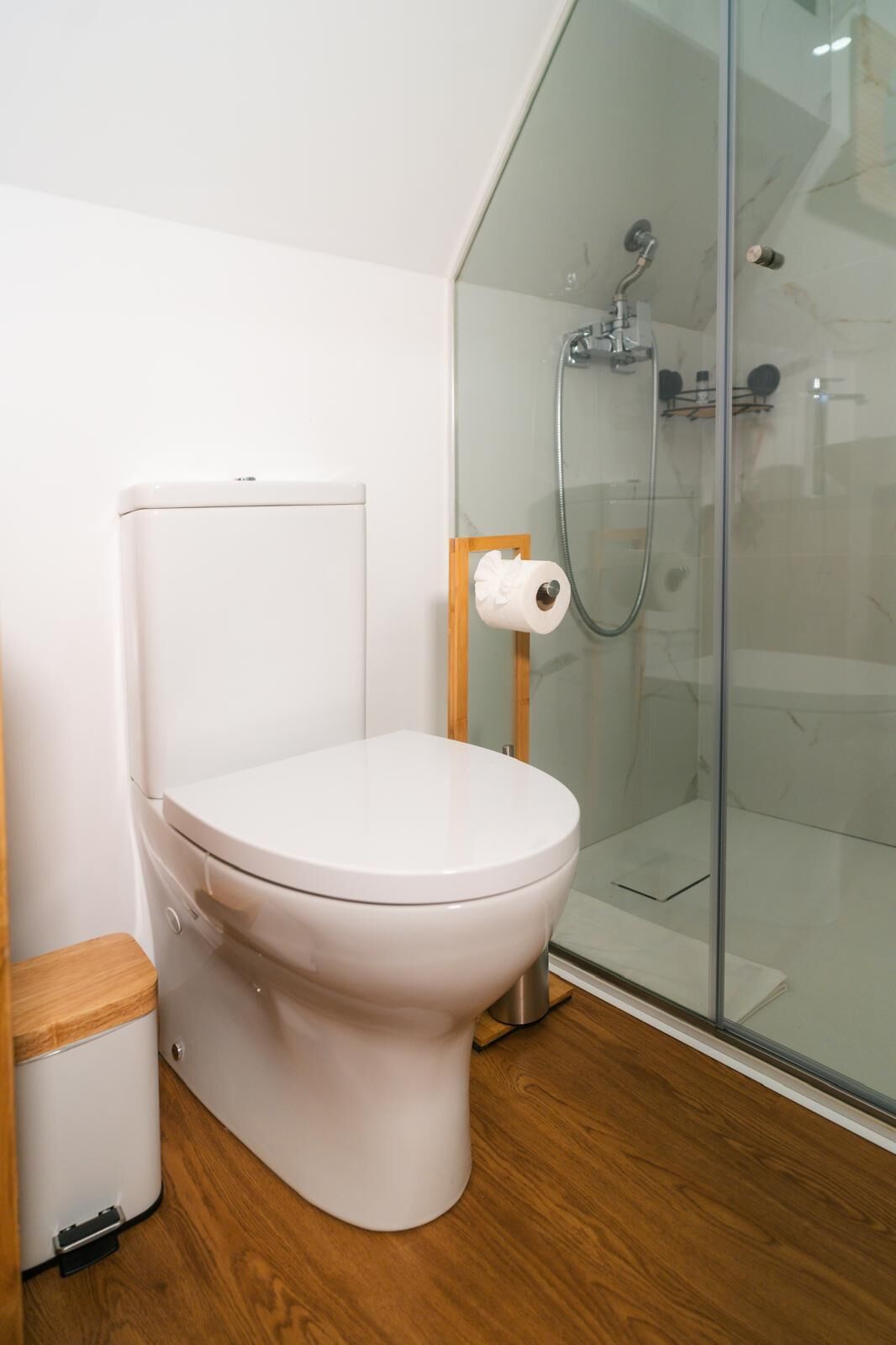 Un baño moderno con inodoro blanco, cabina de ducha de vidrio y suelo de madera.