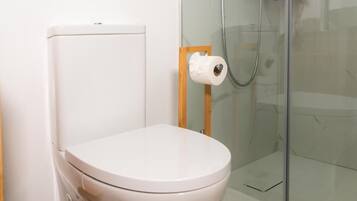 Un baño moderno con inodoro blanco, cabina de ducha de vidrio y suelo de madera.
