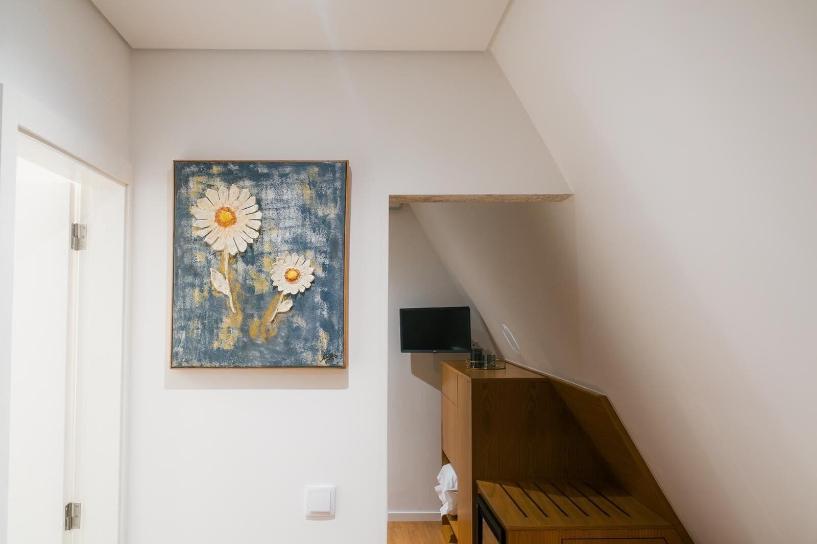 Una stanza con una scala in legno, una porta bianca e un quadro floreale appeso al muro.