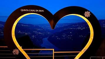 Um sinal em formato de coração com o texto 'QUINTA CASAL DA SILVA' e vista para o horizonte urbano à noite.
