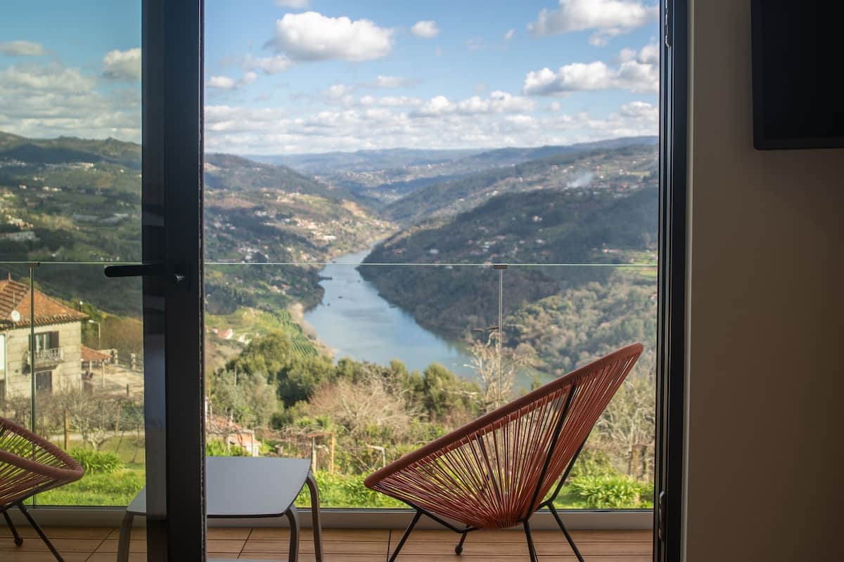 Ein Zimmer mit einer Schiebetür zu einem Balkon mit Blick auf einen Fluss und Hügel.