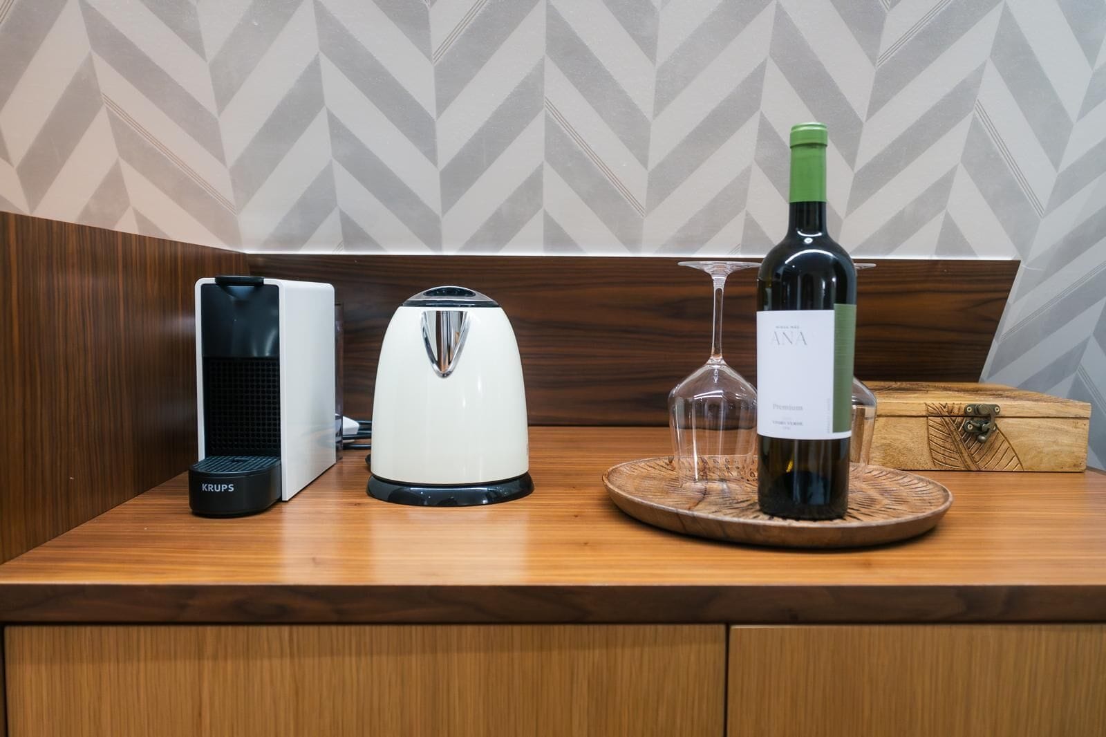 A kitchen counter with a coffee maker, a toaster, a wine bottle, and a glass on a wooden tray.
