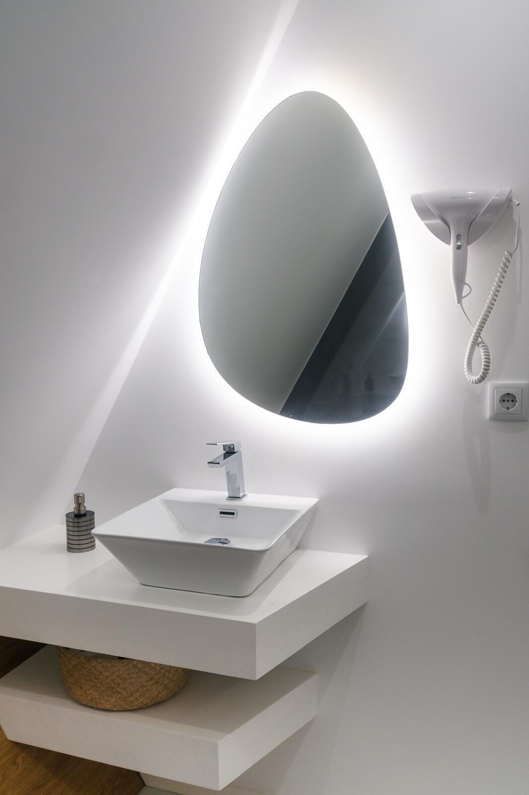 A modern bathroom with a white vanity, a large oval mirror, and a wall-mounted hairdryer.