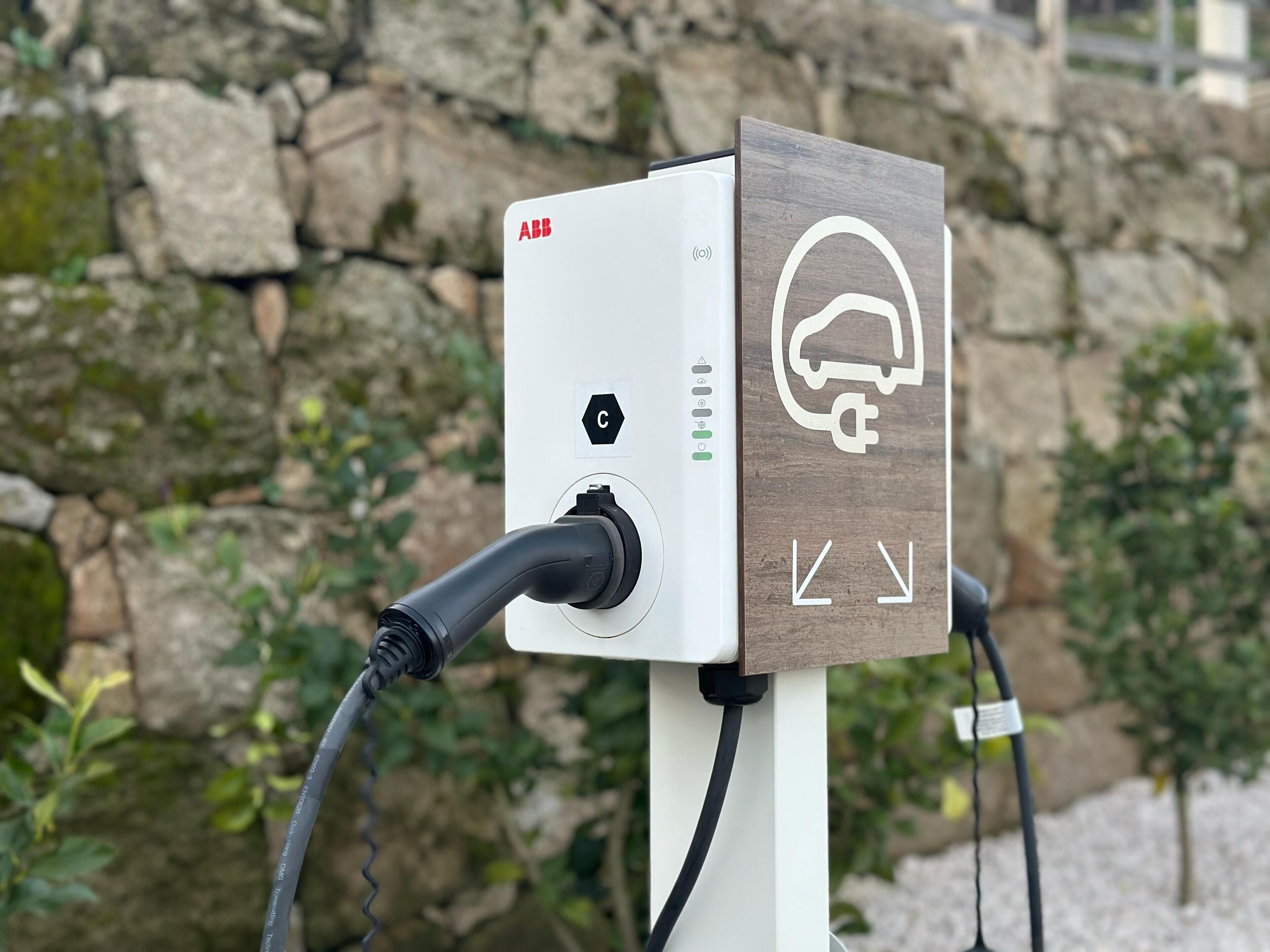Uma estação de carregamento para veículos elétricos com design em branco e madeira, apresentando um plugue e um símbolo de carregamento.
