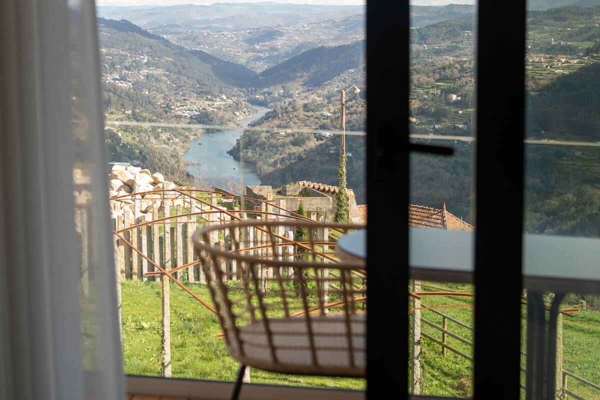 Ein Balkon mit Blick auf einen Fluss und Berge, ein Stuhl und ein Tisch.