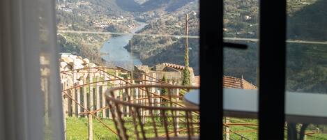 Un balcón con vista a un río y montañas, una silla y una mesa.