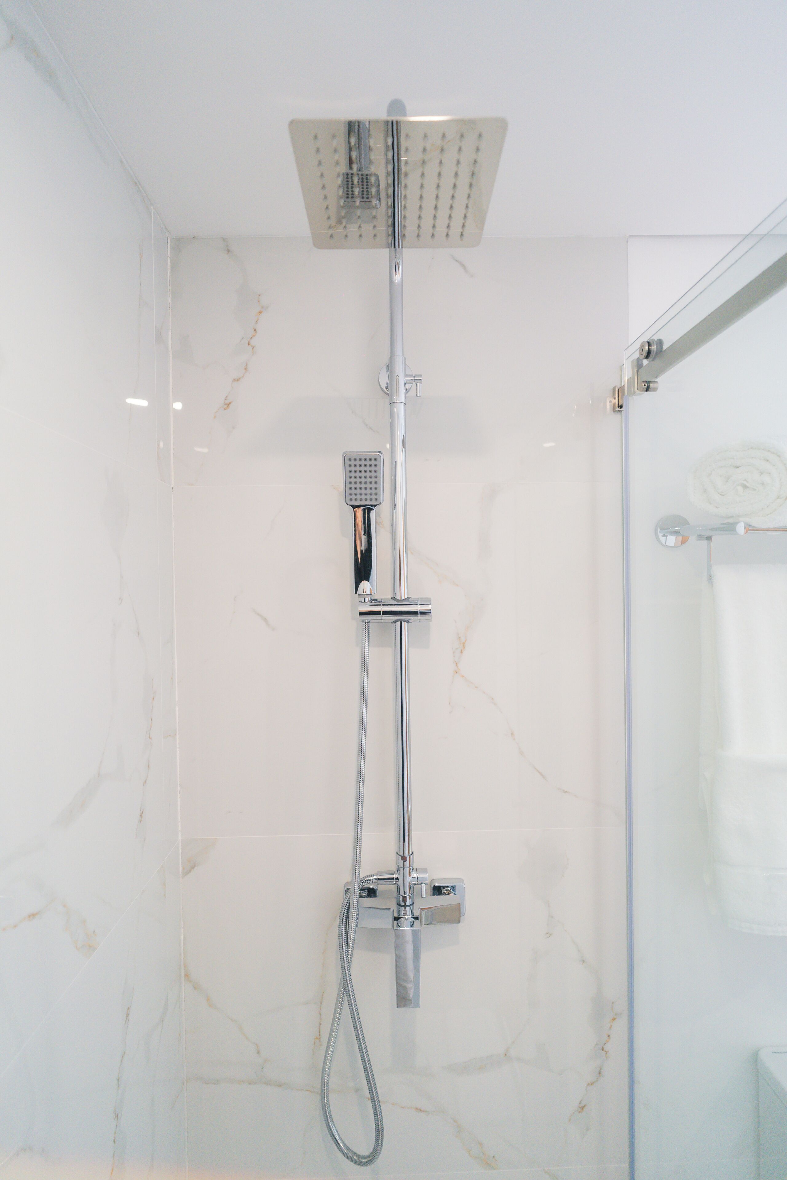 A modern bathroom with a glass-enclosed shower, a handheld showerhead, and a wall-mounted control panel.