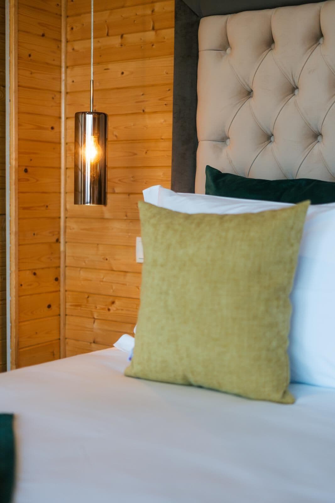 Una cama con un cojín verde y un cabecero capitonado en una habitación con paredes de madera y una lámpara colgante.