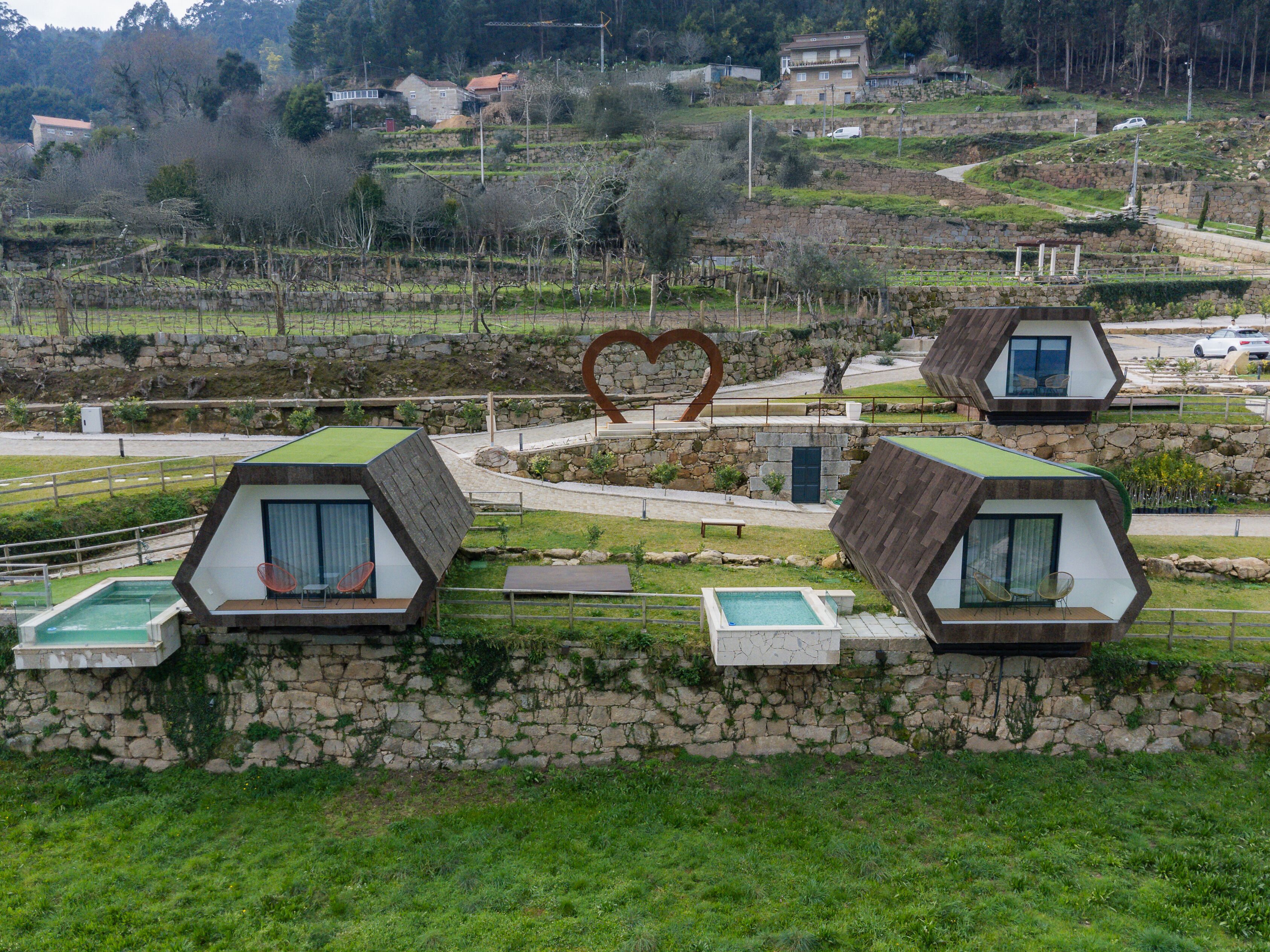 A modern, hexagonal-shaped building with a stone exterior and green roofs, featuring a heart-shaped sculpture in the center.
