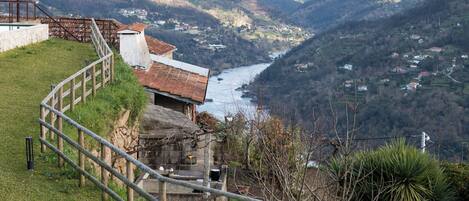 A hillside view overlooking a river valley with a rustic building and a metal railing.