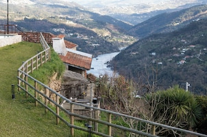 Vista desde una ladera con vista a un valle fluvial, una construcción rústica y una barandilla metálica.