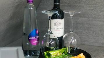 A minibar setup with a bottle of Duas Quintas wine, a bottle of monchiquo, two glasses, and a snack package.
