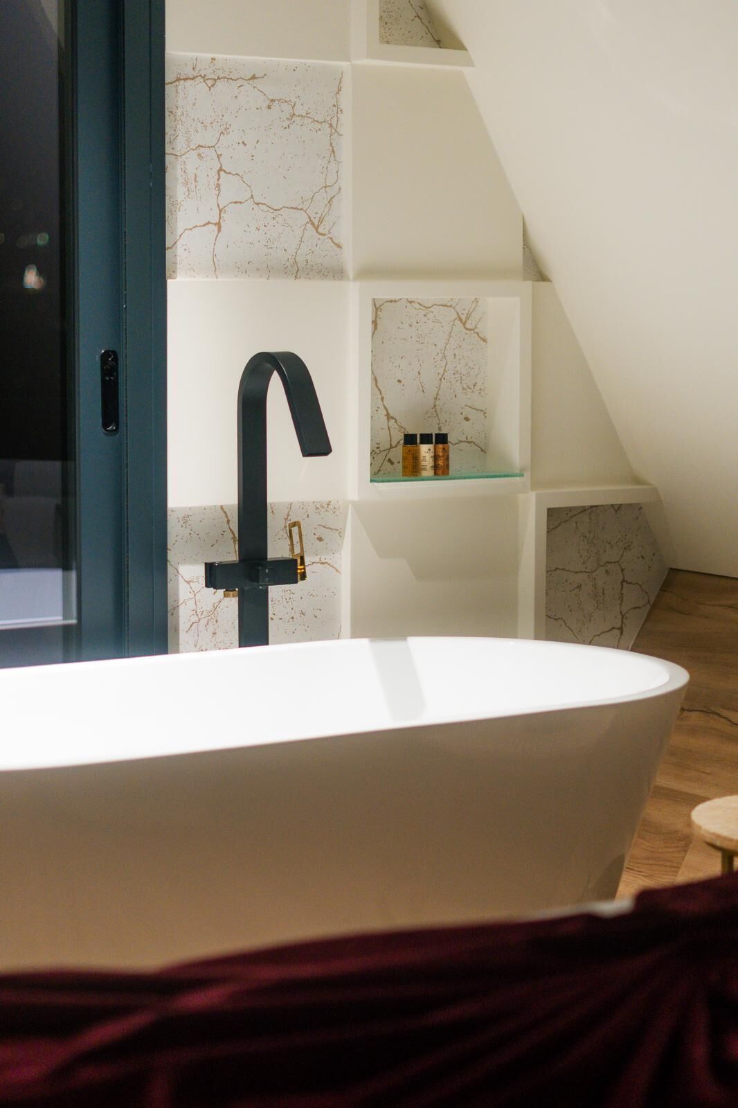 A modern bathroom with a freestanding bathtub, a black faucet, and a shelf with toiletries.