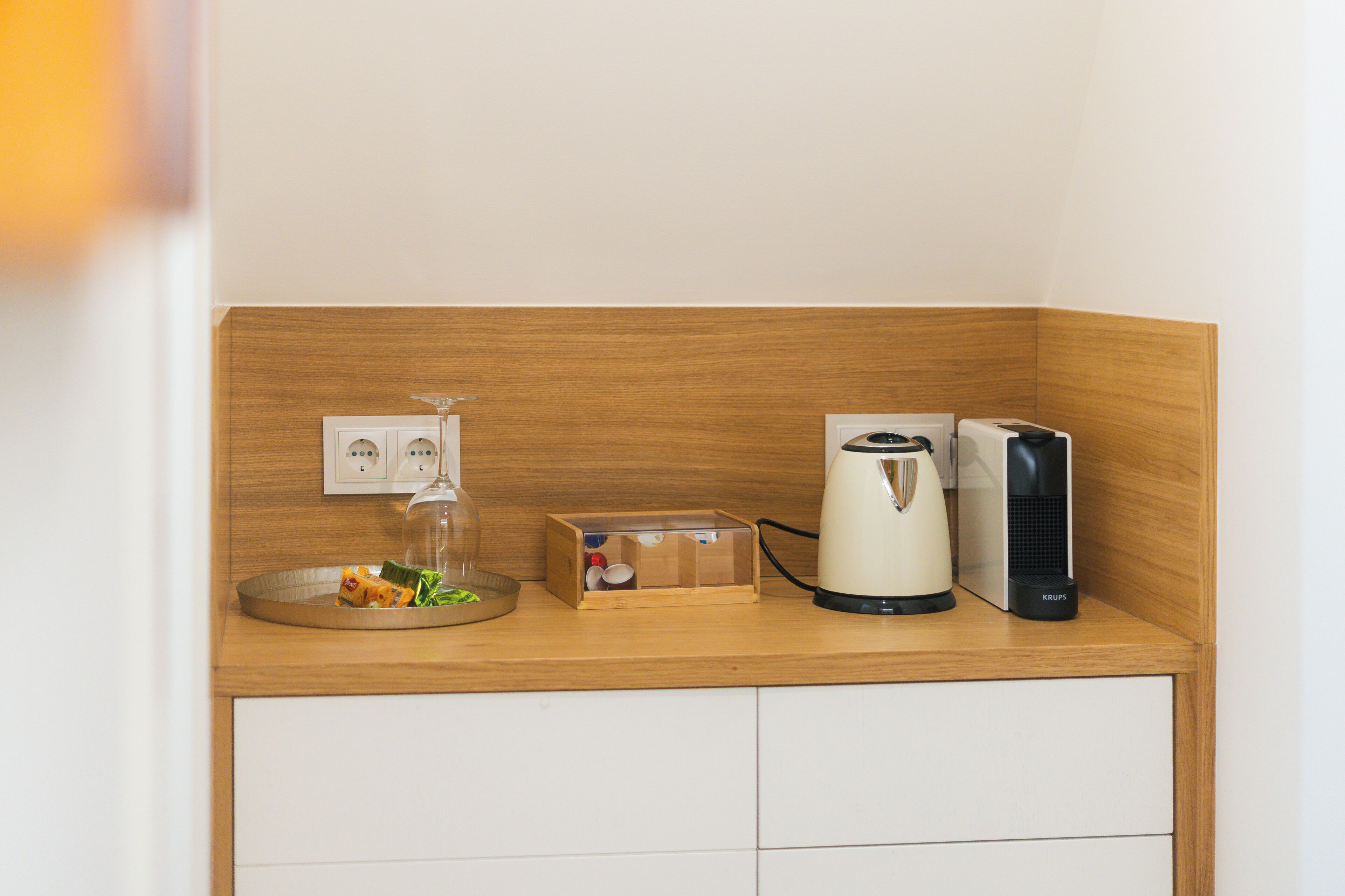 A kitchenette with a coffee maker, a kettle, and a food storage box.