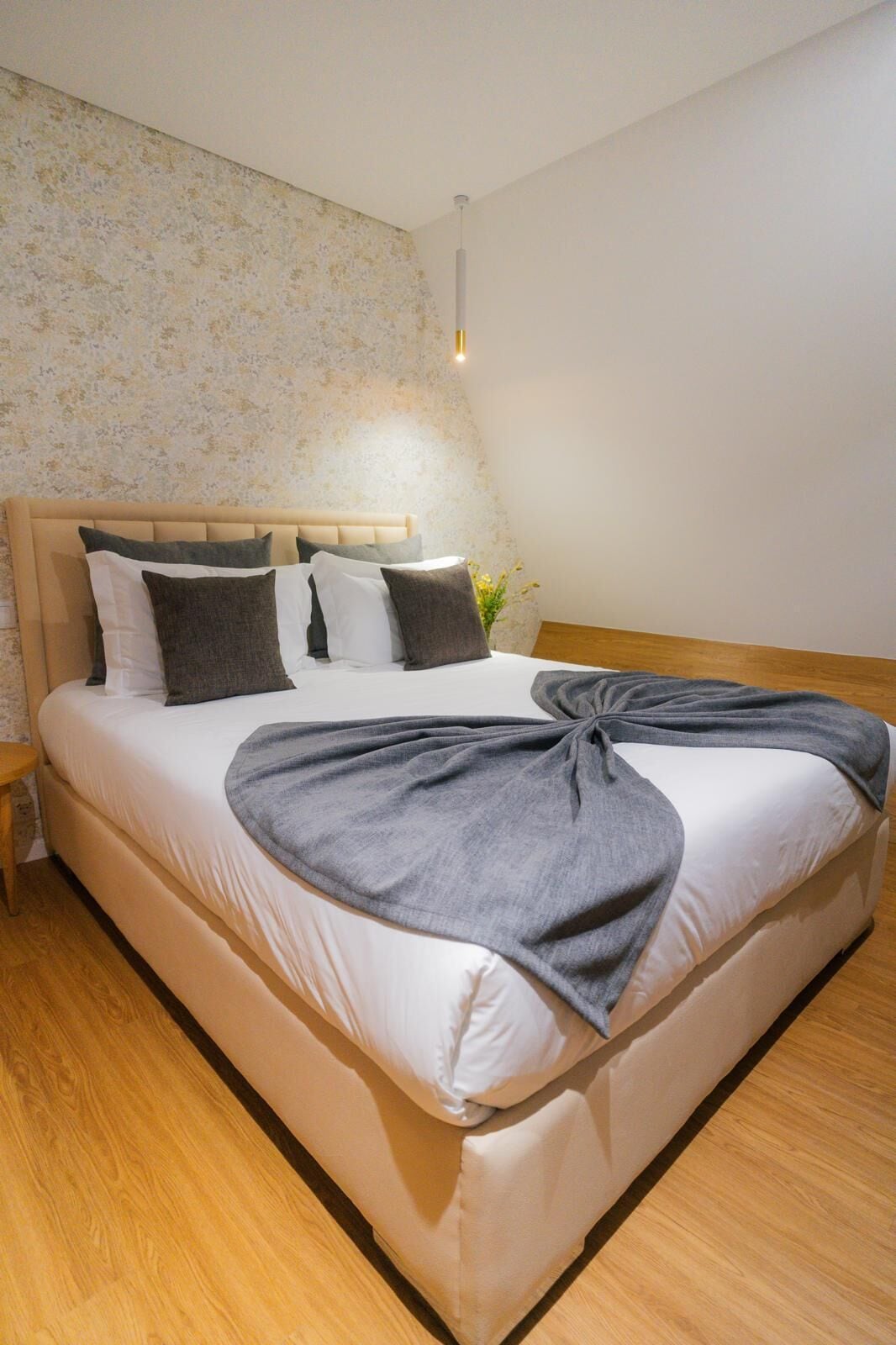 Ein ordentlich bezogenes Bett mit grauer Decke, einem Holzkopfbrett und einem kleinen Nachttisch.