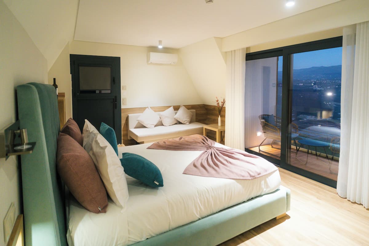 Ein modernes Hotelzimmer mit einem großen Bett, einem Fernseher und einem Balkon mit Blick auf die Stadt.
