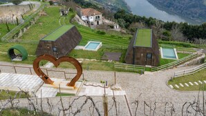 A view of a valley with a river, a small building with a green roof, and a heart-shaped sculpture. - Quinta Casal da Silva 1951 (Marco de Canaveses)