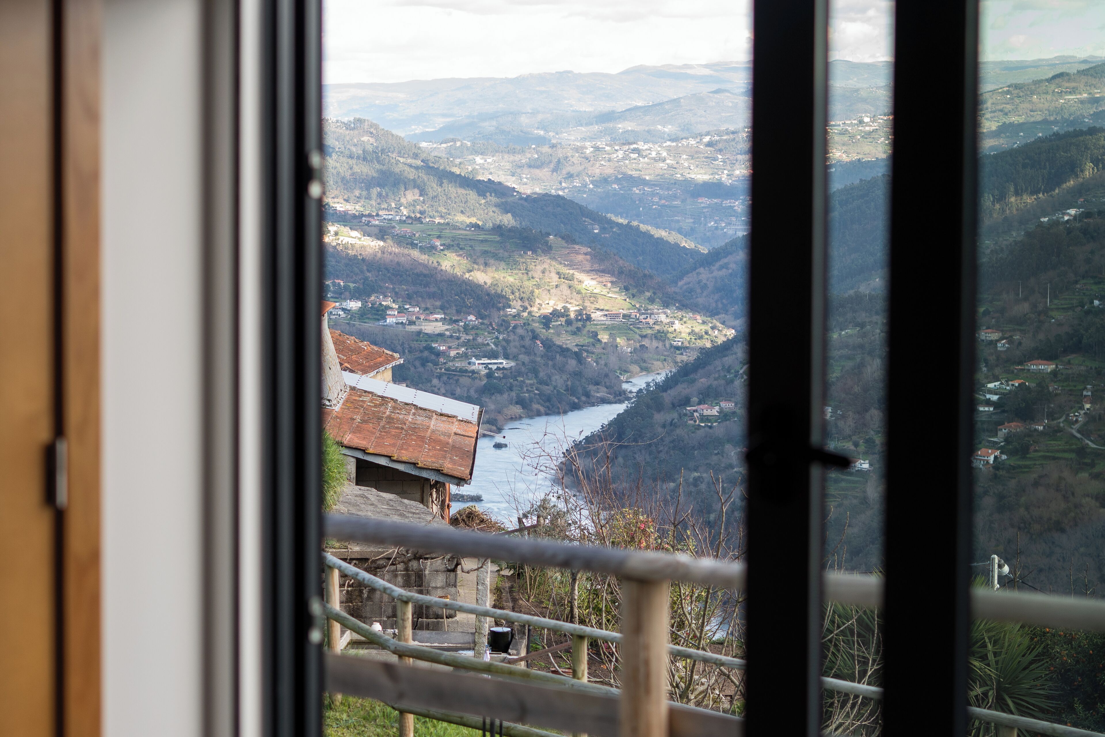 Vista a través de una ventana de un valle con un río, rodeado de colinas y edificios.