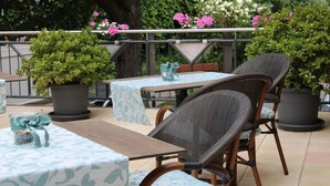An outdoor patio area with wicker chairs and tables, surrounded by potted plants and a railing.