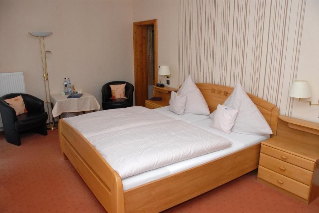 A hotel room with a large bed, a chair, a small table with a lamp, and a nightstand with a lamp.