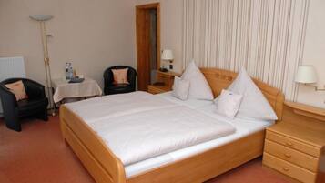 A hotel room with a large bed, a chair, a small table with a lamp, and a nightstand with a lamp.